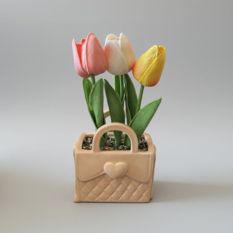 Bomboniera a forma di borsetta in ceramica color pesca con trama trapuntata e cuore, contenente tre tulipani artificiali rosa, bianco e giallo.