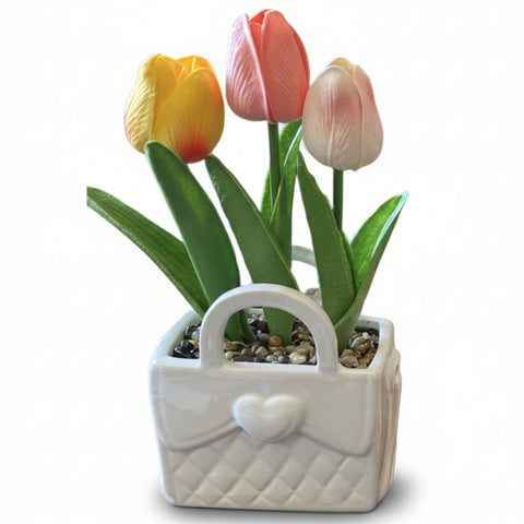 Bomboniera con vaso in ceramica bianca a forma di borsetta trapuntata con cuore centrale, contenente tre tulipani artificiali giallo, rosa e pesca con sassolini.