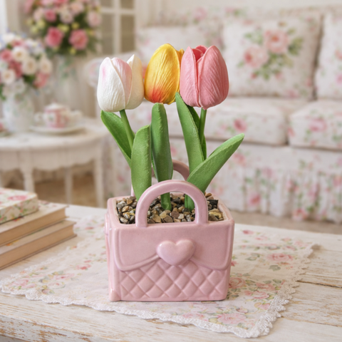 Bomboniera con vaso in ceramica rosa a forma di borsetta trapuntata con cuore, contenente tre tulipani artificiali bianco, giallo e rosa con sassolini decorativi.