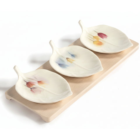 Set antipastiera composto da tre ciotoline in porcellana bianca a forma di foglia con decorazioni floreali di tulipani colorati, posizionate su una base rettangolare in legno chiaro di bambù.