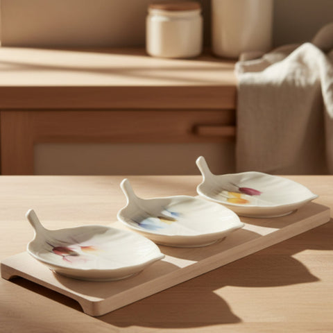 Set antipastiera composto da tre ciotoline in porcellana bianca a forma di foglia con decorazioni floreali di tulipani colorati, posizionate su una base rettangolare in legno chiaro di bambù.